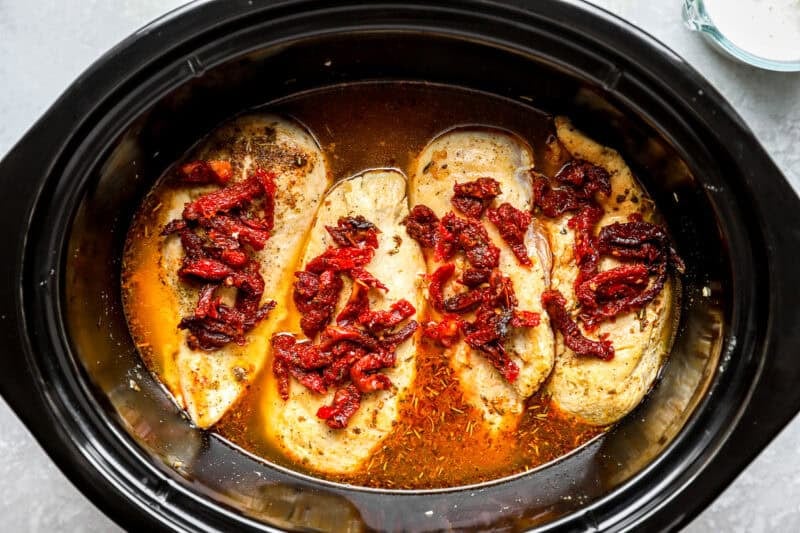Chicken breasts in a slow cooker, topped with sun-dried tomatoes.