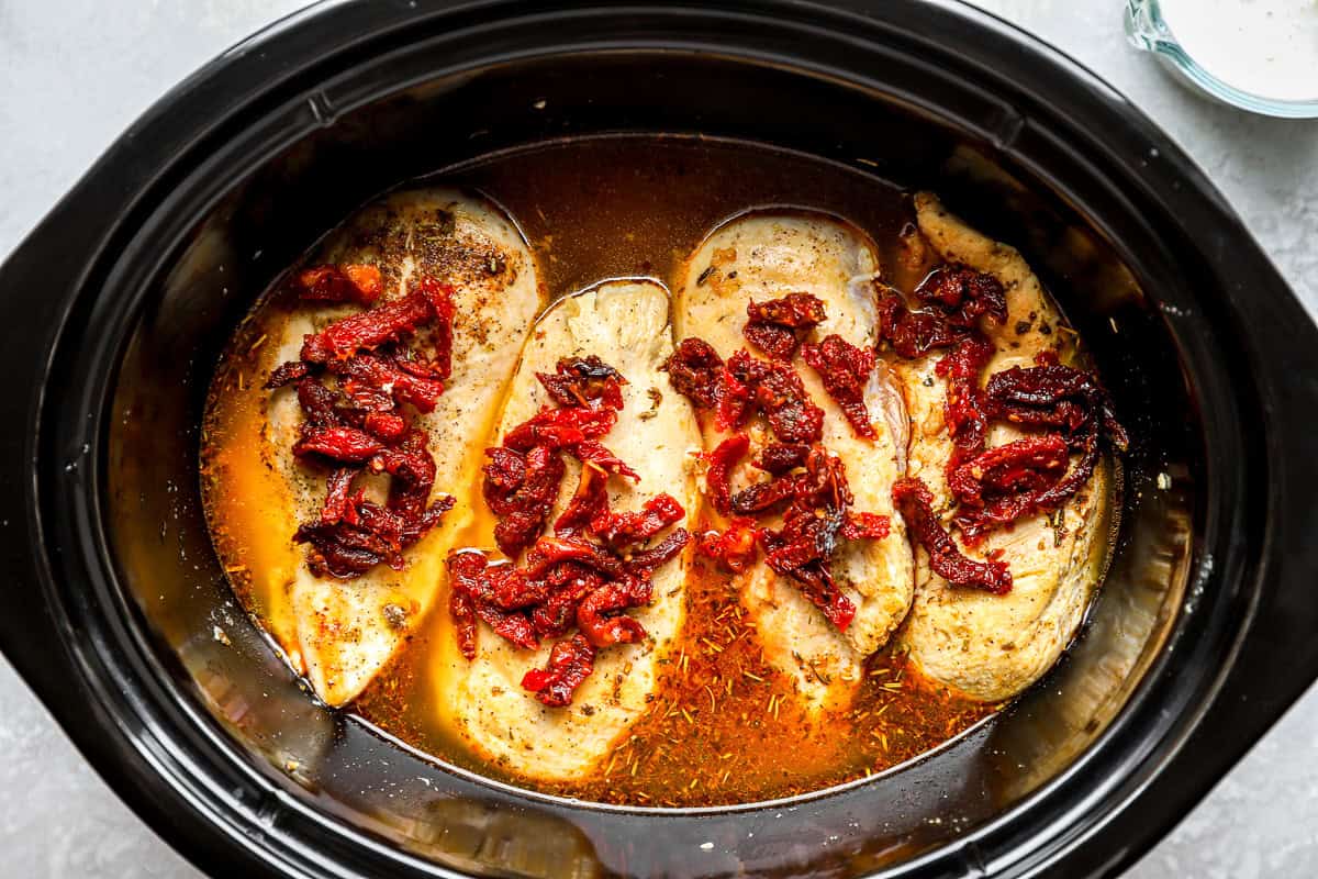 Chicken breasts in a slow cooker, topped with sun-dried tomatoes.
