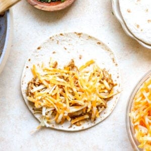 Assembling chicken taco with cheese on a flour tortilla.