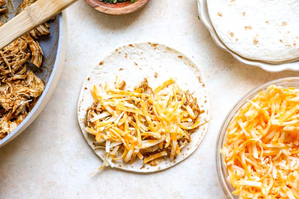 Assembling chicken taco with cheese on a flour tortilla.
