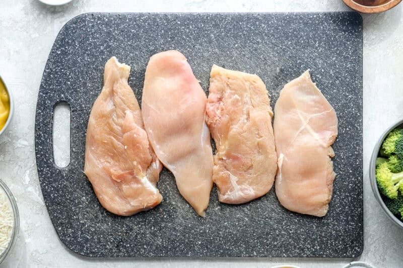 Thinly-sliced chicken breasts lined up on a cutting board.