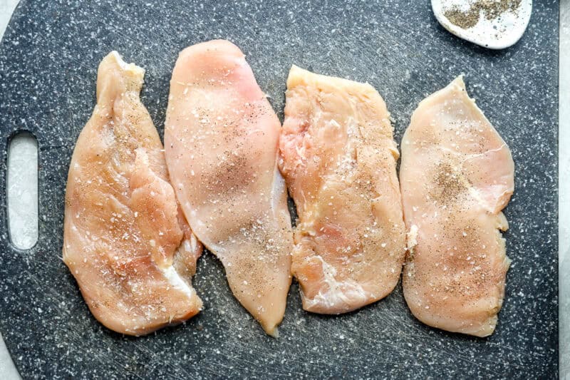 Seasoned chicken breasts on a cutting board.