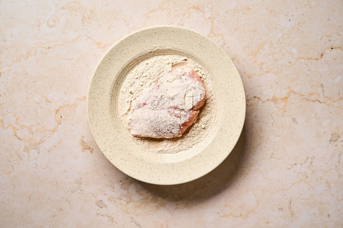 Dredging chicken cutlet in flour.