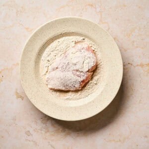 Dredging chicken cutlet in flour.
