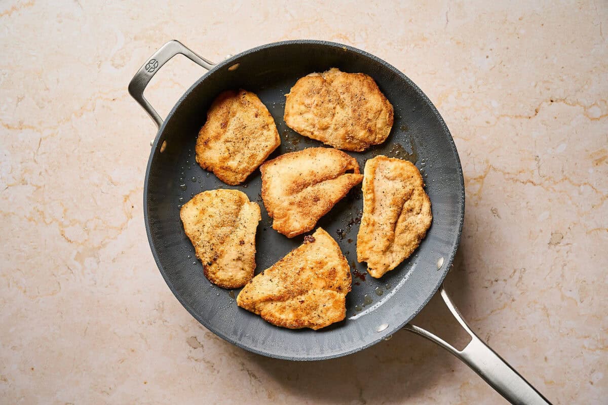 Seared chicken cutlets in a pan.