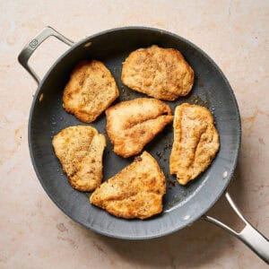Seared chicken cutlets in a pan.