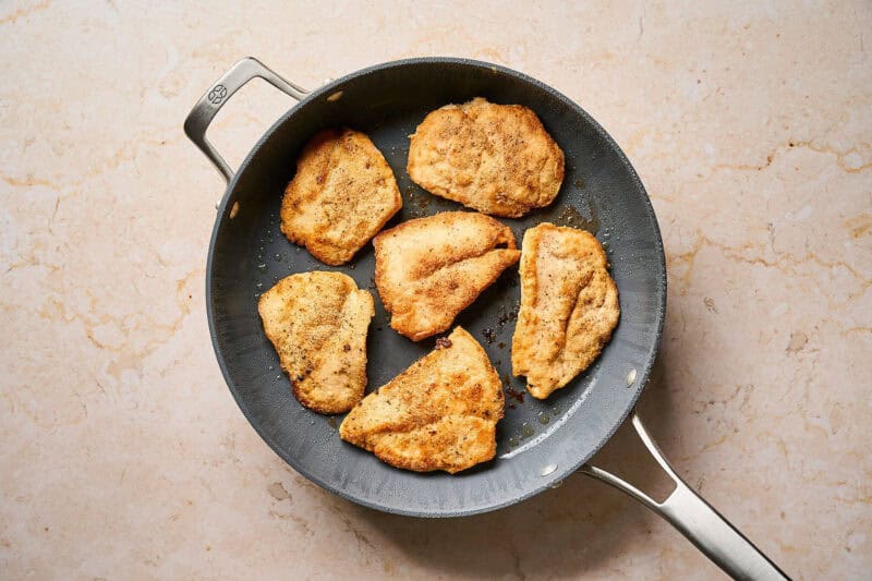 Seared chicken cutlets in a pan.