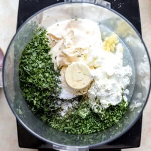 Combining fresh herbs and dressing ingredients in a food processor.