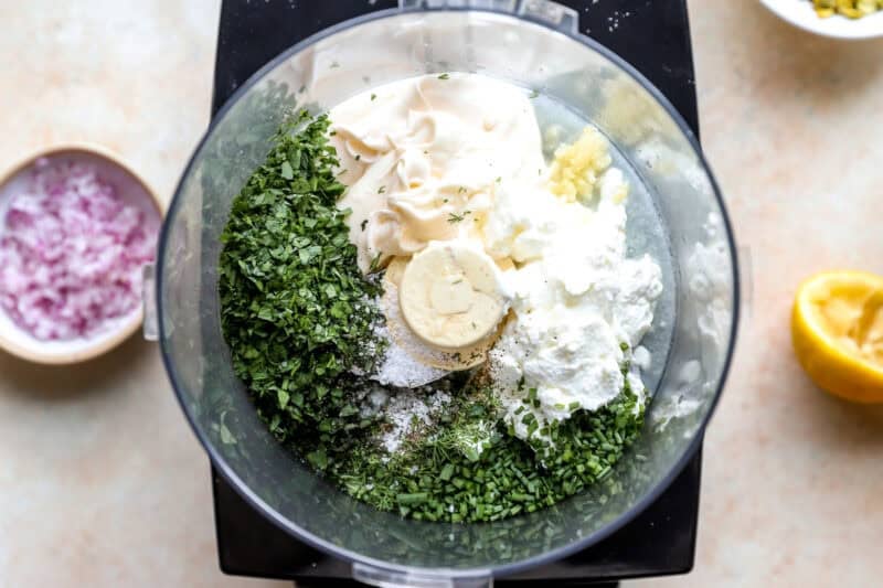 Combining fresh herbs and dressing ingredients in a food processor.