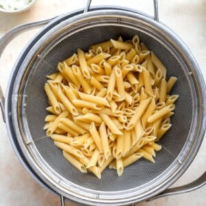 Cooked penne pasta draining in a colander.