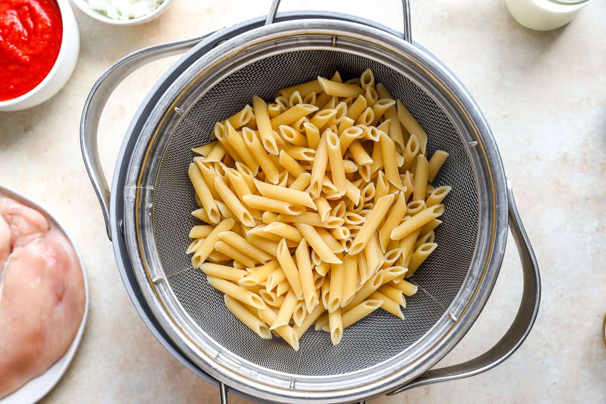Cooked penne pasta draining in a colander.