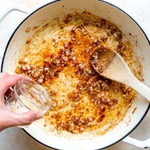 Adding water to a pot of sauteed onion and garlic.