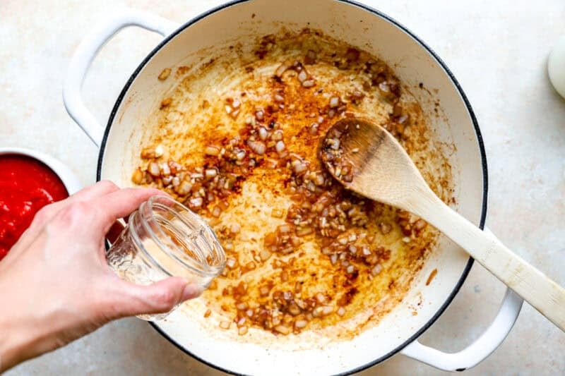 Adding water to a pot of sauteed onion and garlic.
