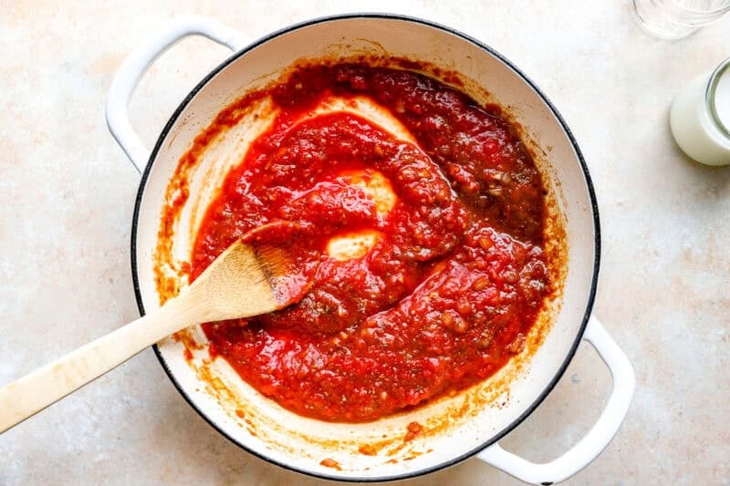 Stirring tomatoes into the pasta sauce.