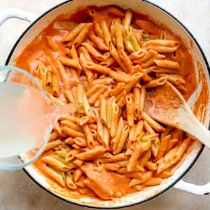 Pouring vodka into the pot of pasta and creamy tomato sauce.