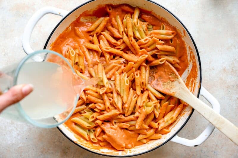 Pouring vodka into the pot of pasta and creamy tomato sauce.