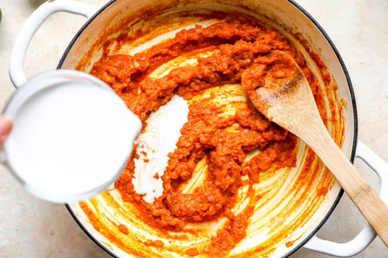 Adding coconut milk to a skillet.