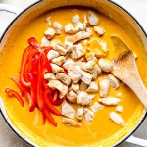 Chicken and peppers added to a pot of pumpkin curry.