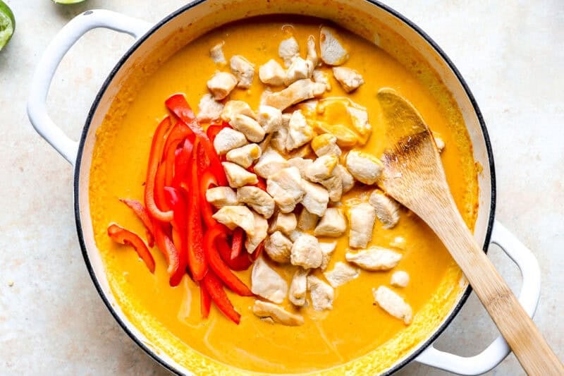 Chicken and peppers added to a pot of pumpkin curry.