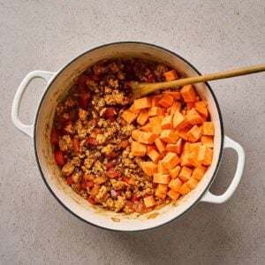 Cubed sweet potatoes added to a pot of ground chicken and veggies.