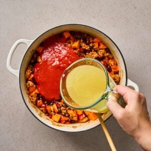 Adding liquid ingredients to a pot of ground meat and veggies.