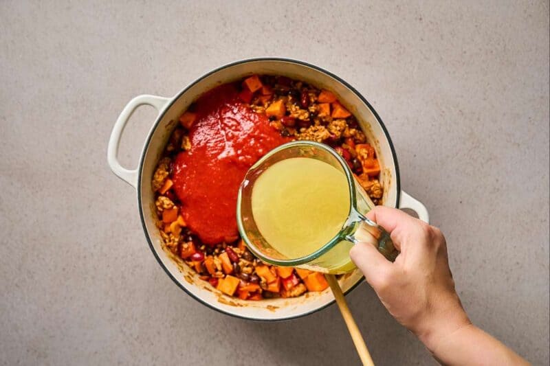 Adding liquid ingredients to a pot of ground meat and veggies.