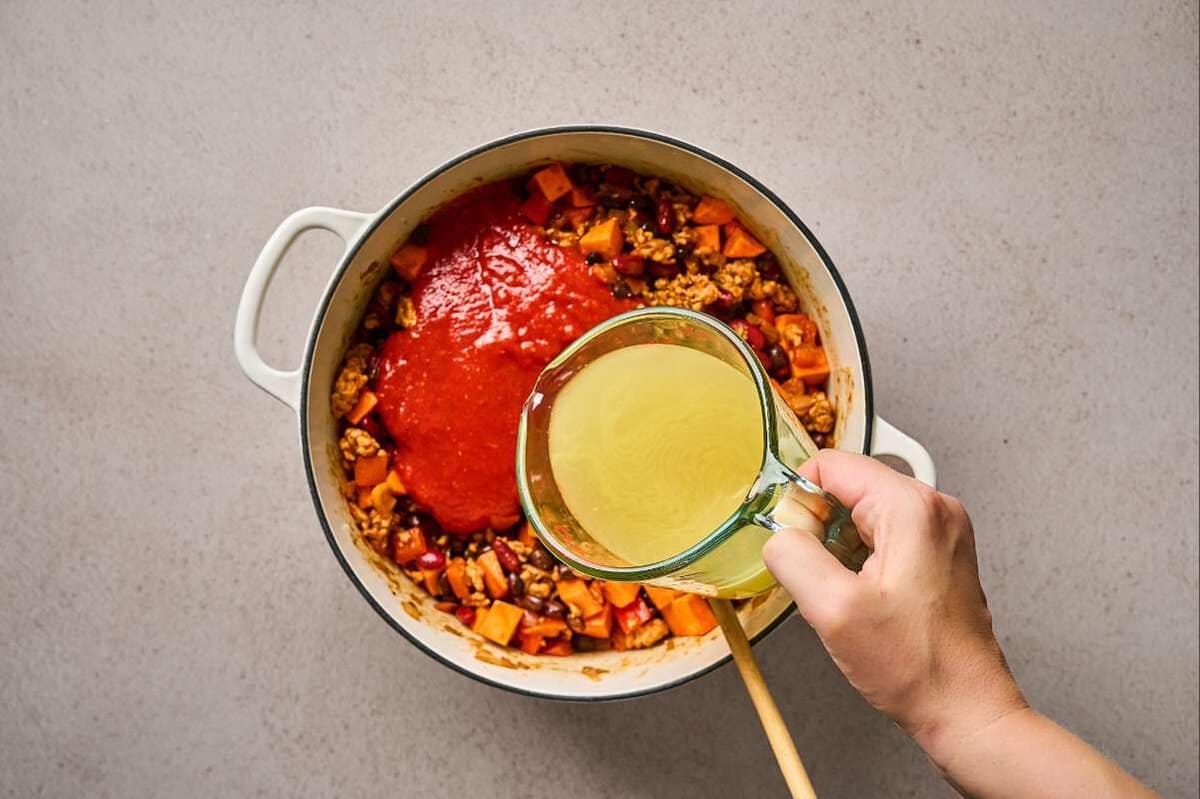 Adding liquid ingredients to a pot of ground meat and veggies.