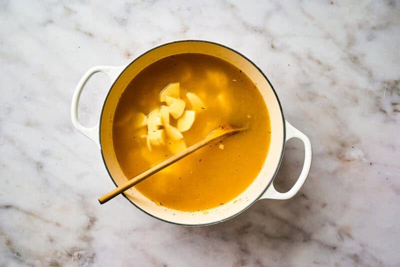Potatoes added to soup broth in a pot.