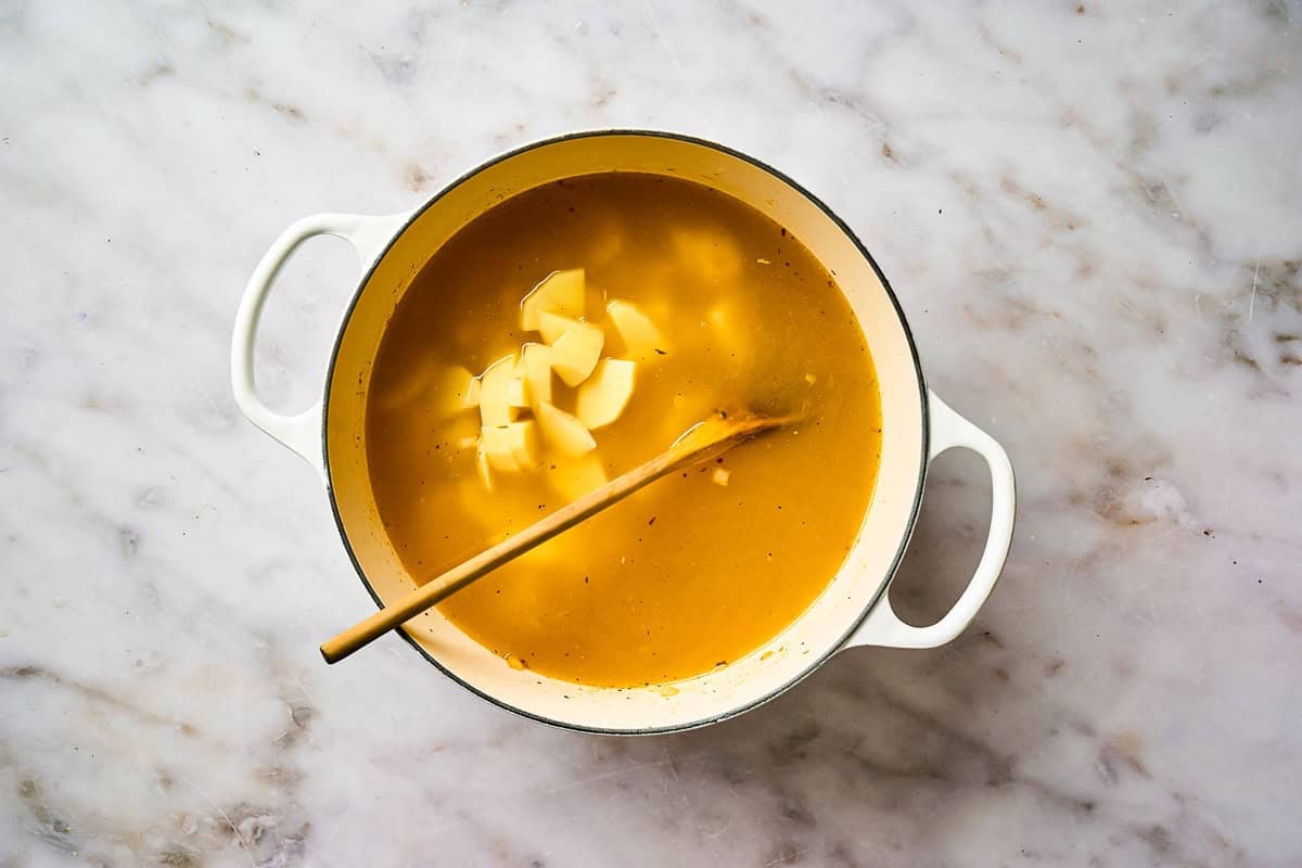 Potatoes added to soup broth in a pot.
