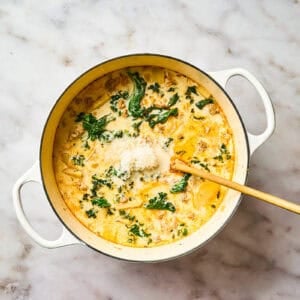 Creamy soup with kale, ground meat, and potatoes cooking in a pot.