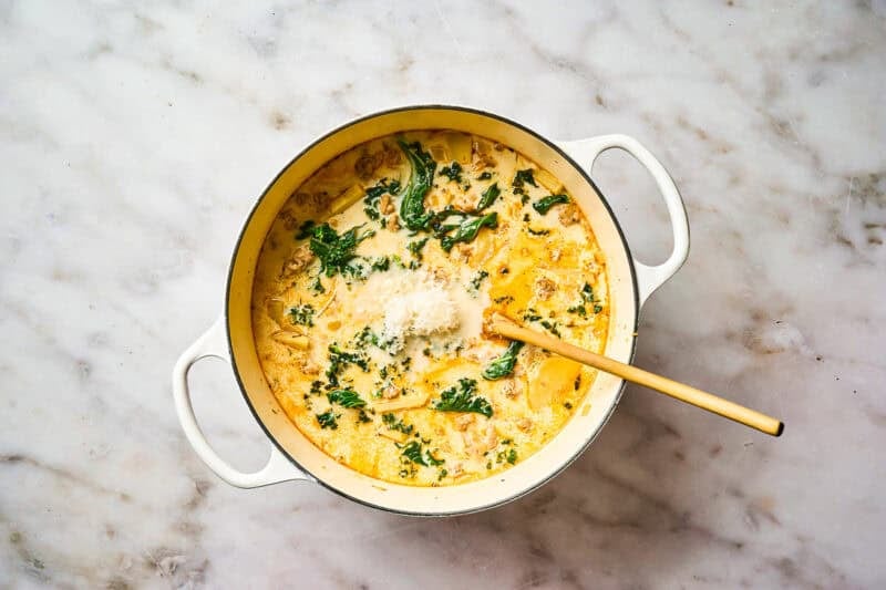 Creamy soup with kale, ground meat, and potatoes cooking in a pot.