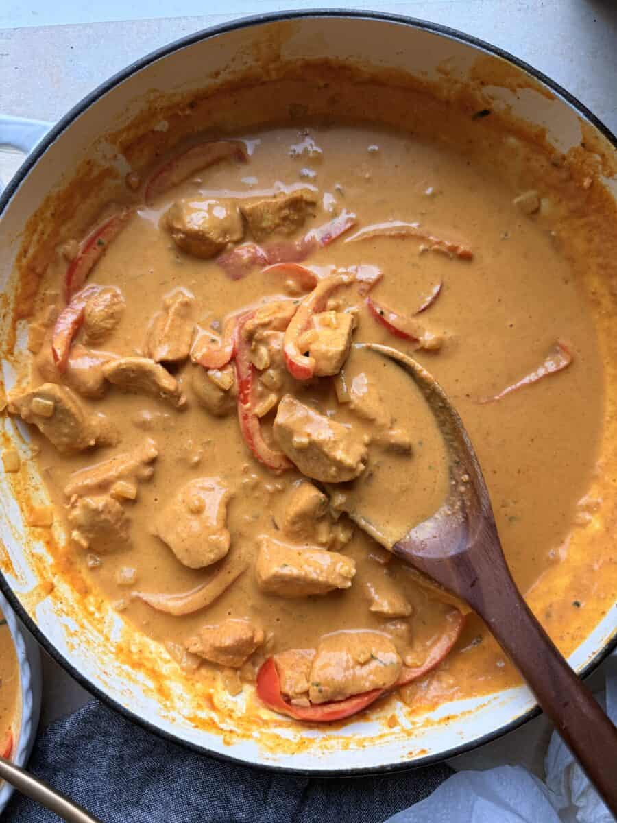 Cooking pumpkin coconut curry in a skillet with chicken.