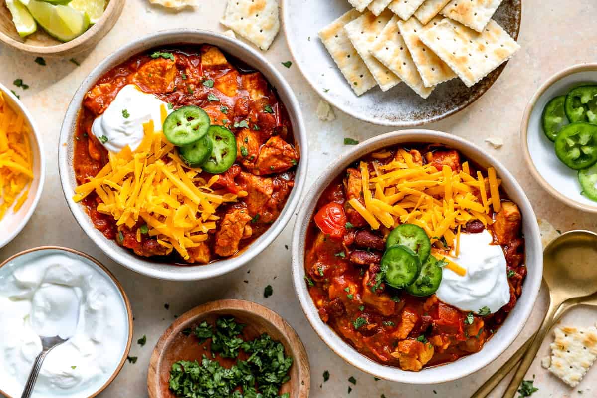 Bowls of red chicken chili topped with cheese, sour cream, and jalapeños.
