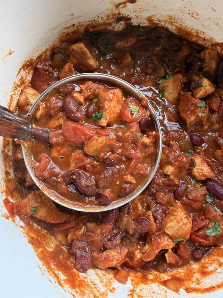 Ladling a portion of chicken chili out of the pot.