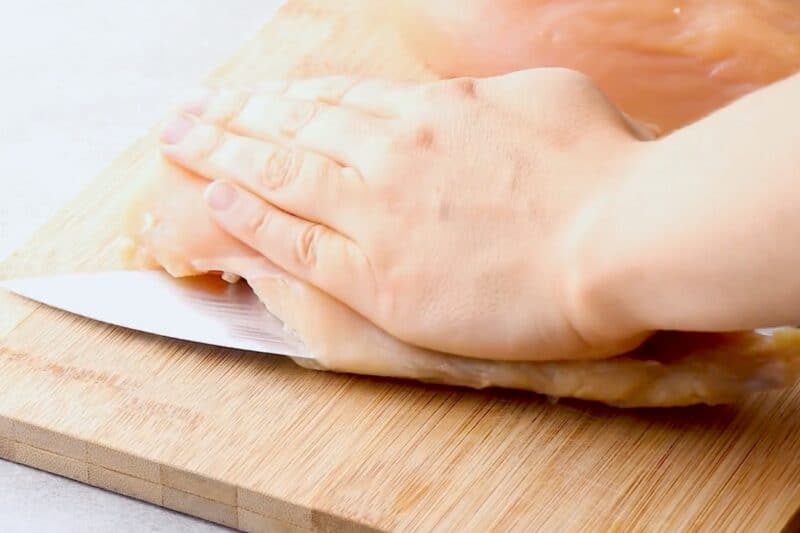Slicing chicken breast in half to create a cutlet.