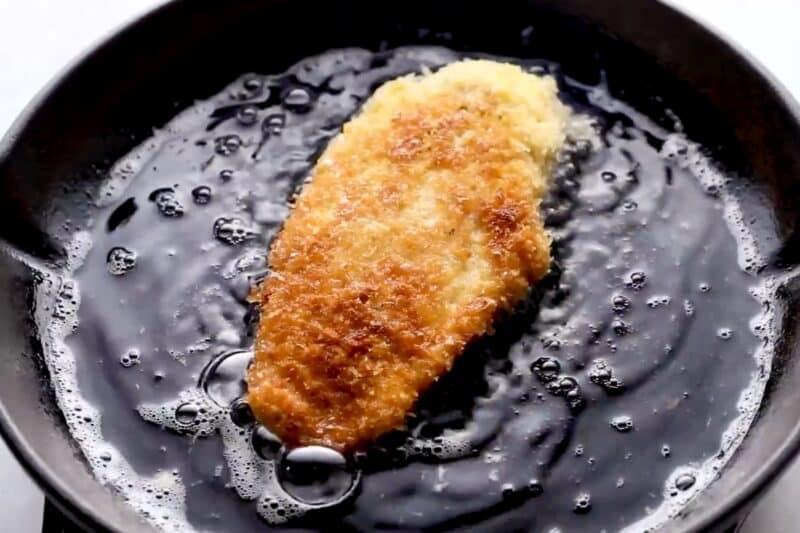 Panko-coated chicken cutlet frying in a pan.