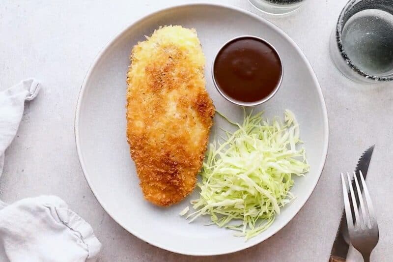 Plated chicken katsu with tonkatsu sauce and shredded cabbage.