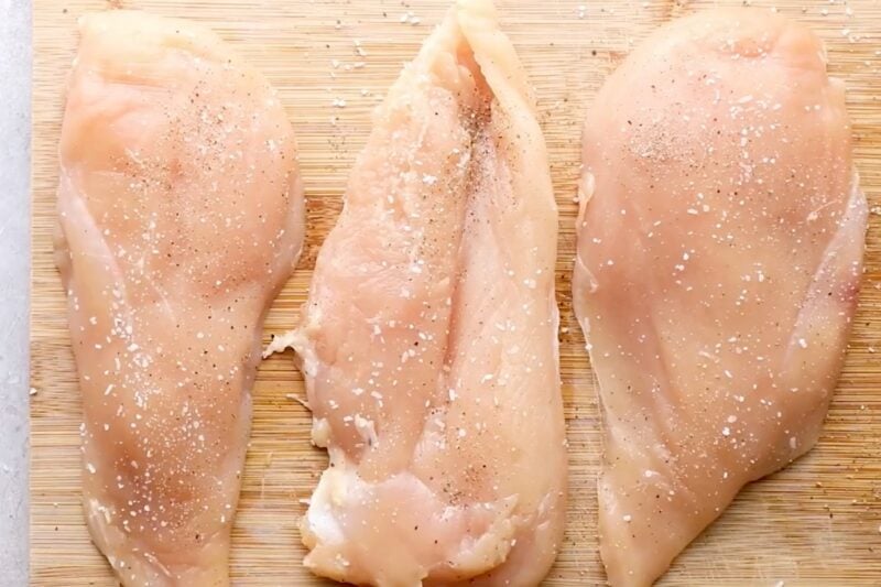 Seasoned chicken cutlets on a cutting board.